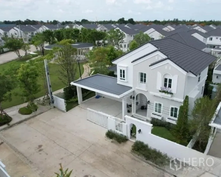 Detached House for rent in Bang Phli, Samut Prakan - Aerial view of a two-storey white detached house with gated driveway, carport and landscaped park in a secure estate.