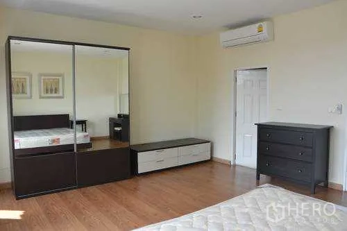 Home Office for rent in Wang Thonglang, Bangkok - Bedroom with mirrored wardrobe, dresser and wall-mounted air conditioner on wood floors in Wang Thonglang.