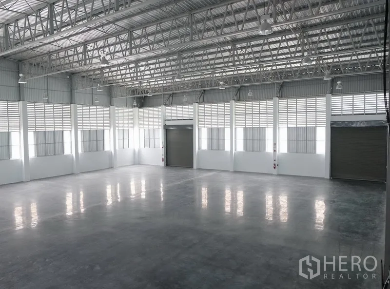 Factory for rent in Bang Sao Thong, Samut Prakan - Spacious warehouse interior with an 8 m high steel truss roof, polished concrete floor and multiple roller shutter entrances.