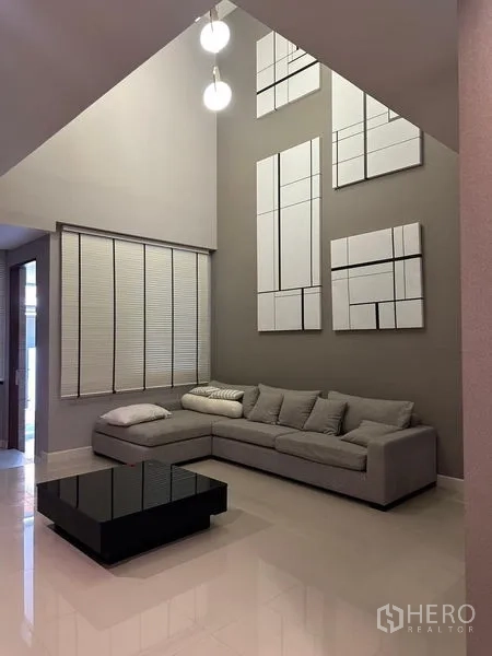 Townhouse for sale in Saphan Sung, Bangkok - Double‑height living area with sectional sofa, tall feature wall and pendant lights.