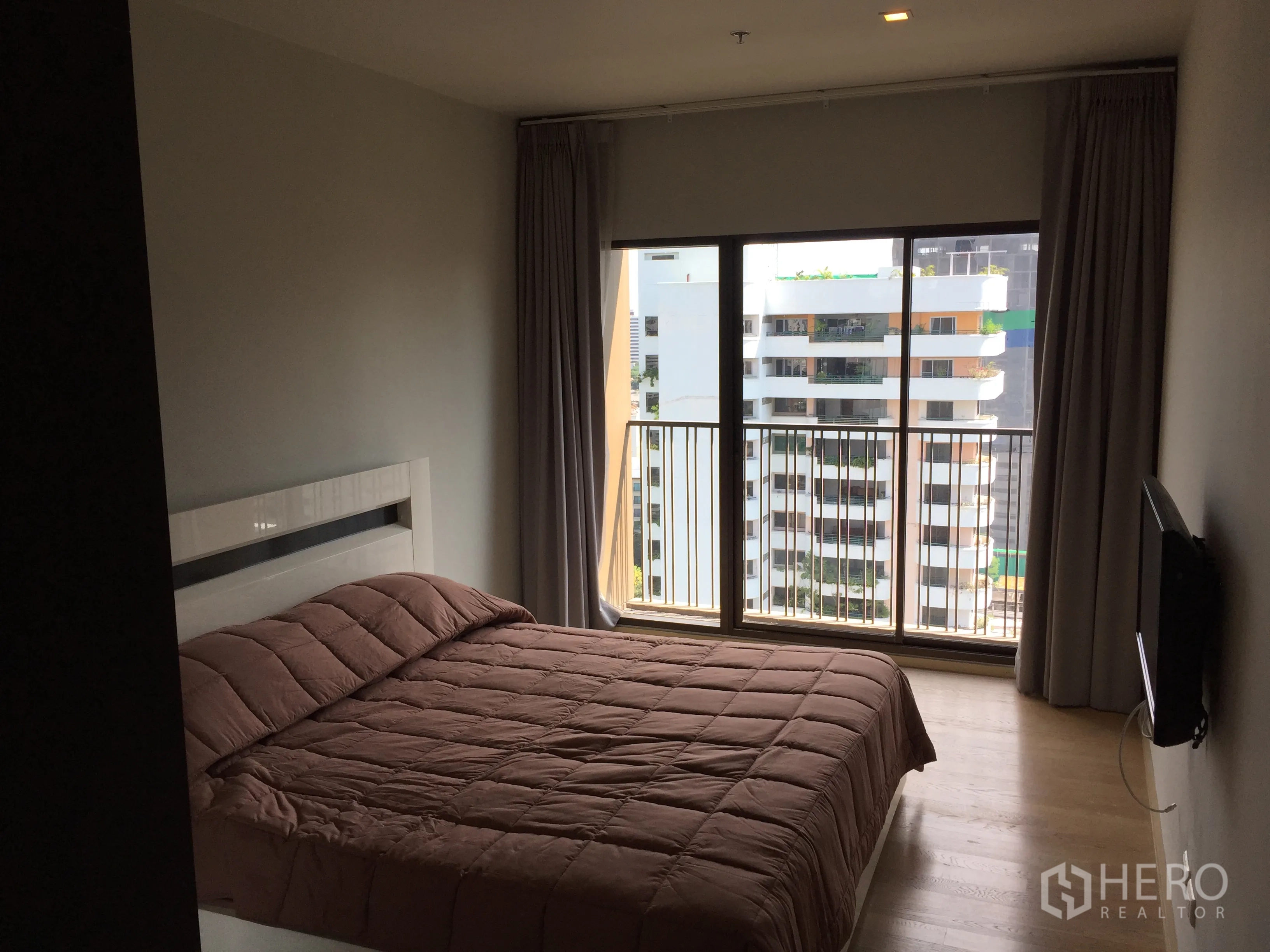 Condominium for rent in Bangkok - Bright bedroom with floor-to-ceiling window, city-view balcony, light wood floors and a taupe duvet.