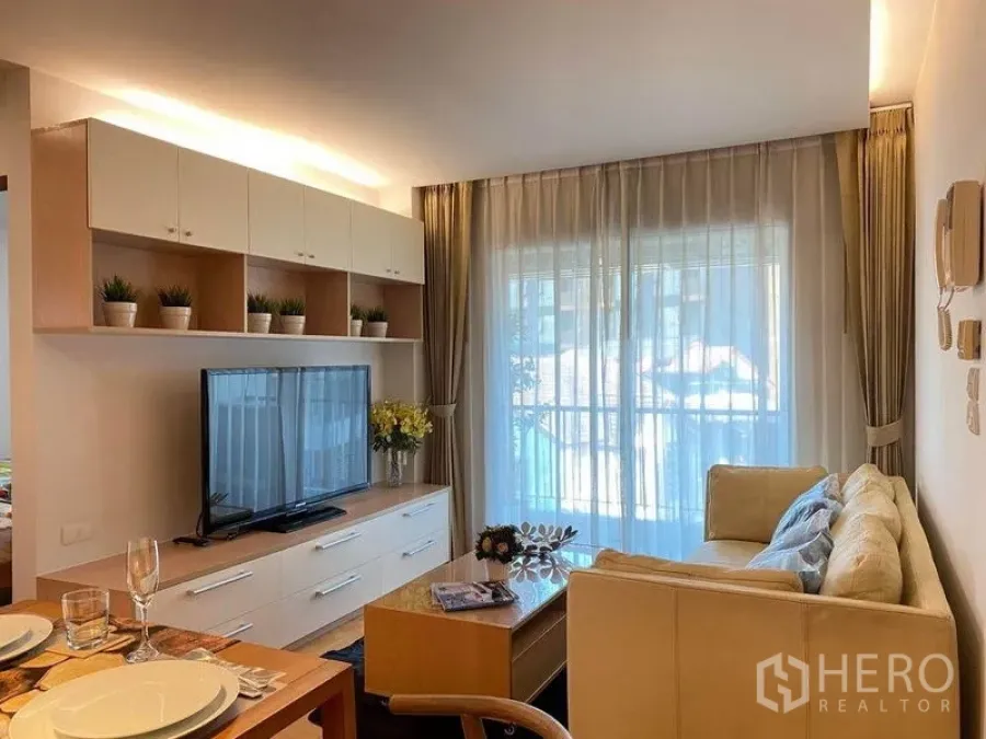 Condominium for rent or sale in Phra Khanong, Bangkok - Bright living room with sofa, TV cabinet, shelving and sliding glass door to balcony.