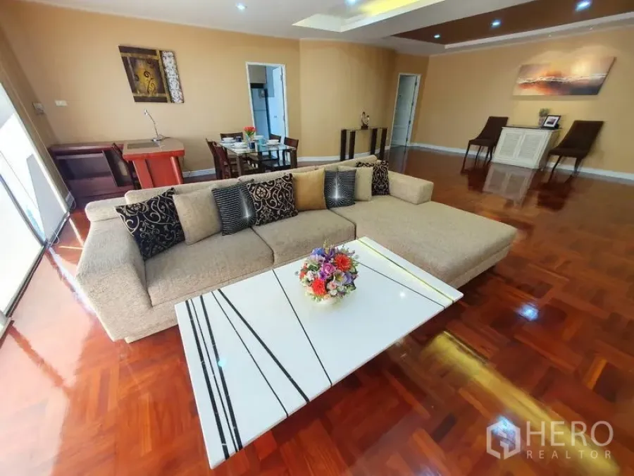 Condominium for rent in Watthana, Bangkok - Spacious living room with L-shaped sofa, white coffee table, and polished hardwood floors.