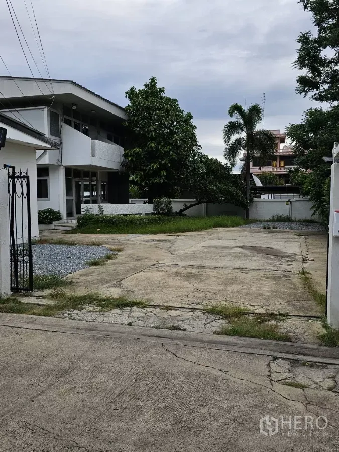Detached House for rent or sale in Lat Phrao, Bangkok - Gated entrance with wide concrete driveway leading to a two-storey white detached house and garden.