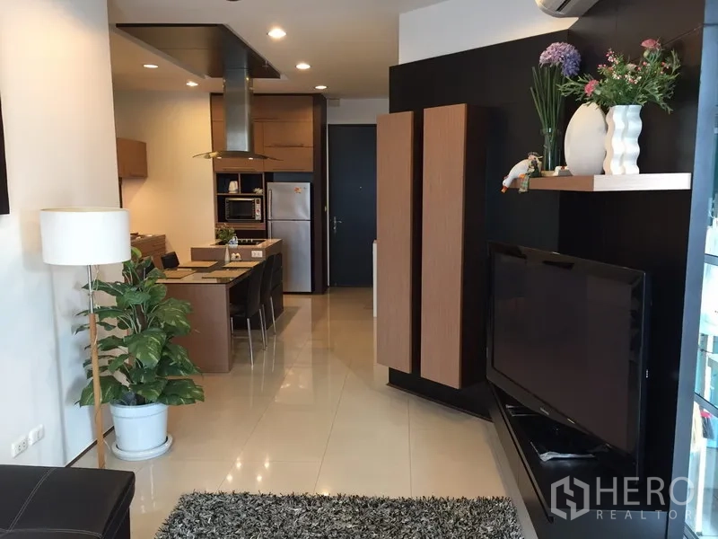 Condominium for rent in Khlong Toei, Bangkok - Open-plan living and dining area with TV wall unit, indoor plants and a cozy rug.