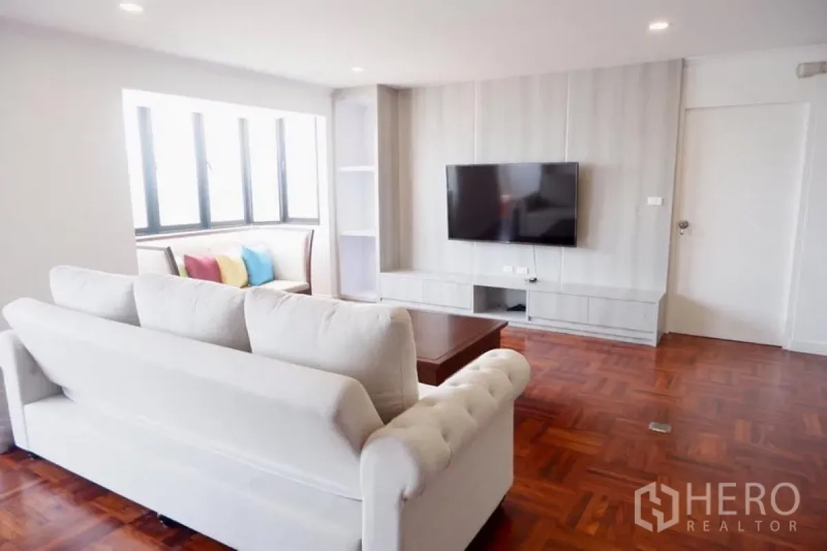 Condominium for rent in Khlong Toei, Bangkok - Cozy lounge view showing white sofa facing mounted TV and a window seat.