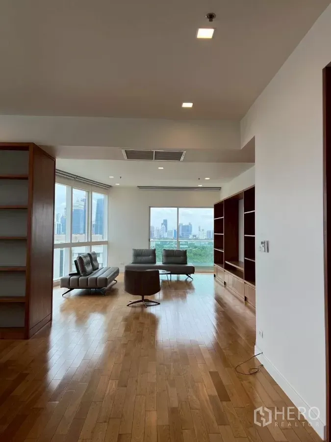 Condominium for rent in Khlong Toei, Bangkok - Bright living room with hardwood floors, built‑in shelving and full-height windows overlooking the Bangkok skyline and park.