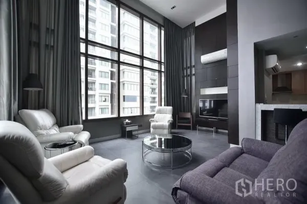 Condominium for rent in Khlong Toei, Bangkok - Bright lounge with floor-to-ceiling windows, leather armchairs and TV wall overlooking neighboring towers.