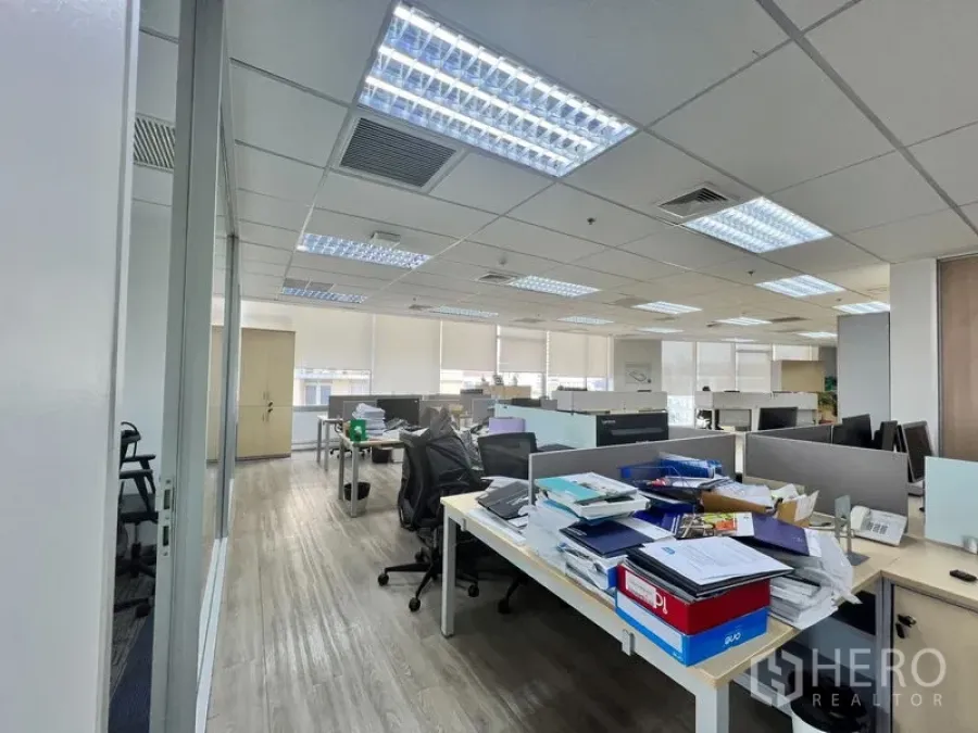 Office Space for rent - Open office zone with desks and paperwork under bright LED lights.