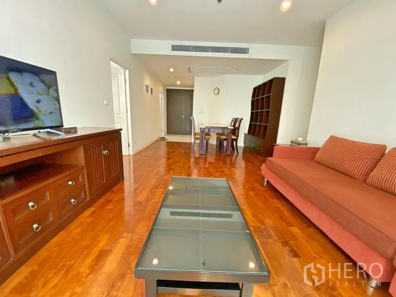 Condominium for rent in Khlong Toei, Bangkok - Open-plan living area with TV console, glass coffee table and wooden flooring.