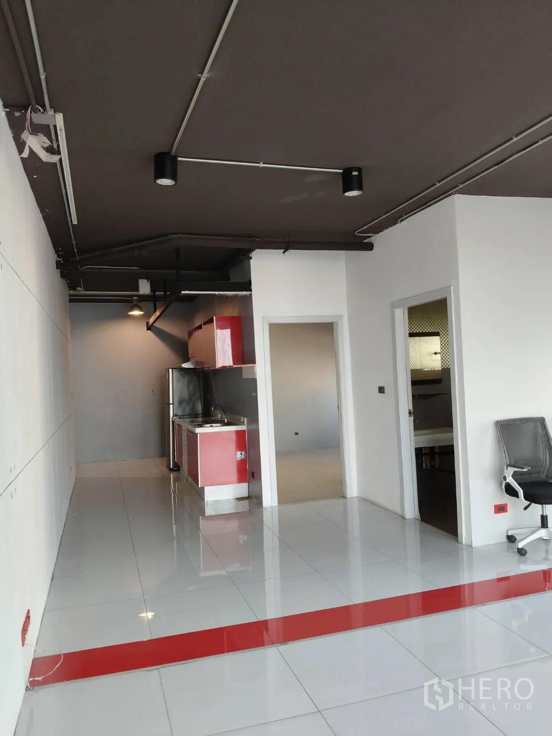 Office Space for rent in Khlong Toei, Bangkok - Entry area showing red kitchenette, doors to rooms and polished white flooring.