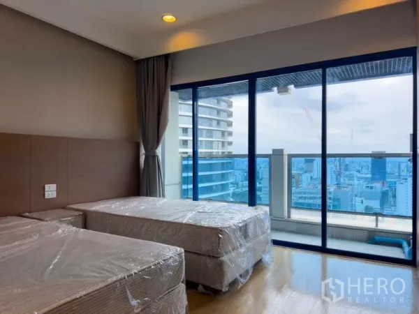 Condominium for rent or sale in Pathum Wan, Bangkok - Bedroom with twin beds and floor‑to‑ceiling windows opening to the balcony.