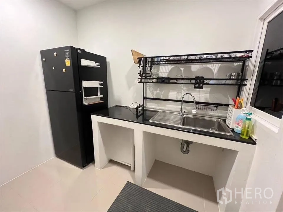 Detached House for rent in Prawet, Bangkok - Kitchen with refrigerator, sink, black countertop and metal dish rack.
