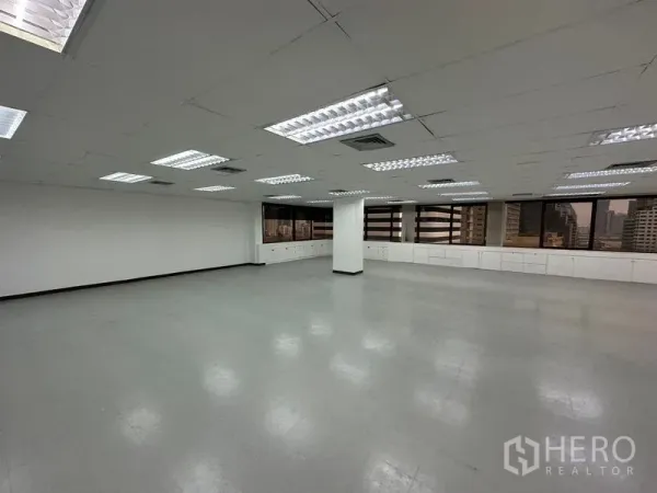 Office Space for rent in Watthana, Bangkok - Open-plan office interior with bright fluorescent lights, white ceiling, built-in low cabinets under wide windows and city views.
