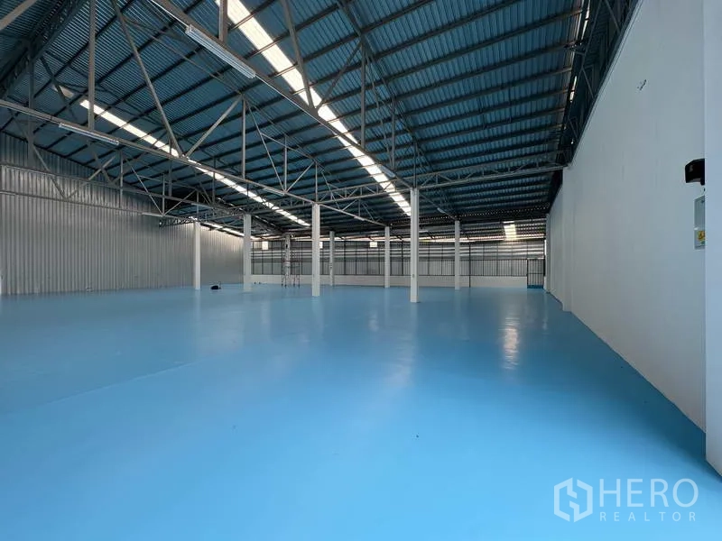 Warehouse for rent in Mueang Pathum Thani, Pathum Thani - Long interior view with white columns, ribbed metal wall panels, and glossy epoxy floor.
