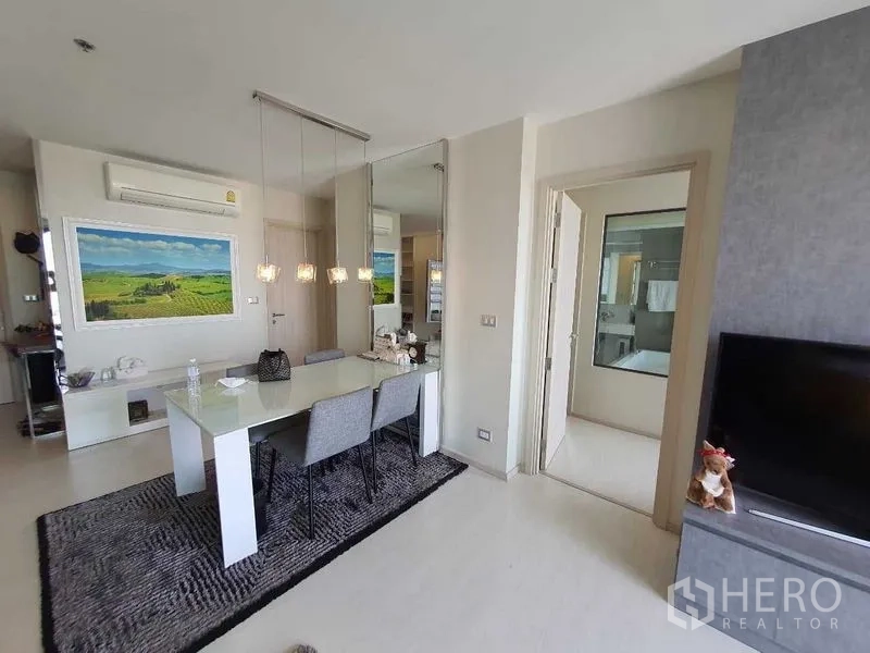 Condominium for sale in Khlong Toei, Bangkok - Bright dining area with pendant lights, a mirror wall, and doorway to the bathroom.