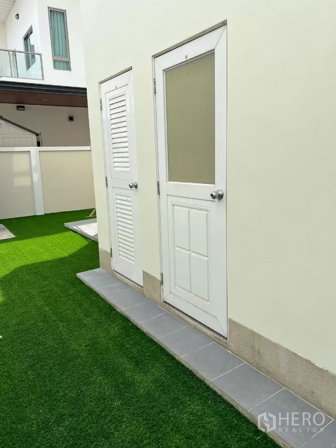 Detached House for rent in Bang Phli, Samut Prakan - Side yard with white service doors and artificial grass