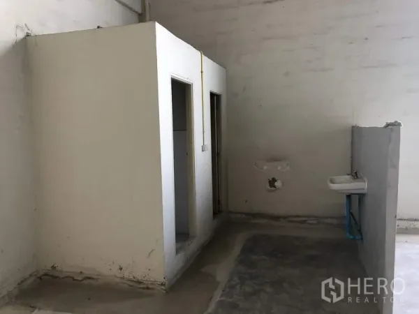 Warehouse for rent in Khlong Luang, Pathum Thani - Basic warehouse restroom area with two toilet cubicles and a wall-mounted sink.