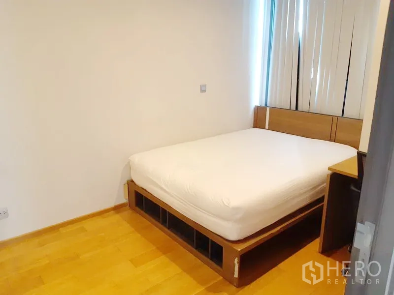 Condominium for sale in Khlong Toei, Bangkok - Cozy bedroom with double bed, wood flooring and window blinds for privacy.