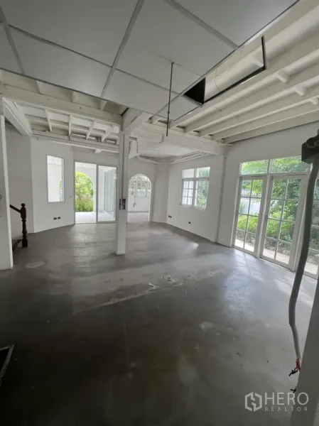 Detached House for rent or sale in Sathon, Bangkok - Spacious ground-floor interior with exposed beams, concrete floor and full-height glass doors to garden.