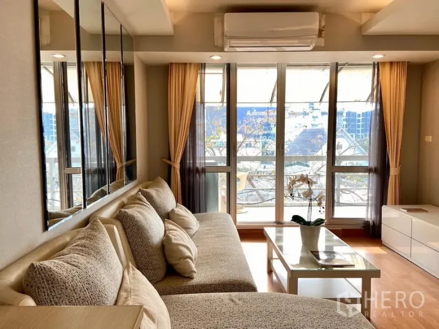 Condominium for sale in Khlong Toei, Bangkok - Bright living room with large windows, balcony access, sectional sofa and coffee table in a Khlong Toei condo near BTS On Nut.