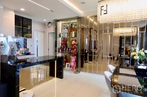 Detached House for rent in Samut Prakan - Living–dining area with mirrored accent wall and illuminated glass display cabinet.