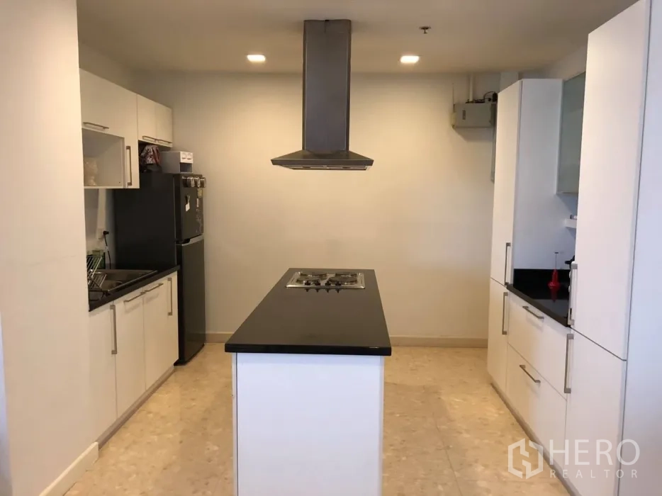 Condominium for sale in Khlong Toei, Bangkok - Full view of the kitchen with island cooktop, tall storage cabinets and refrigerator.