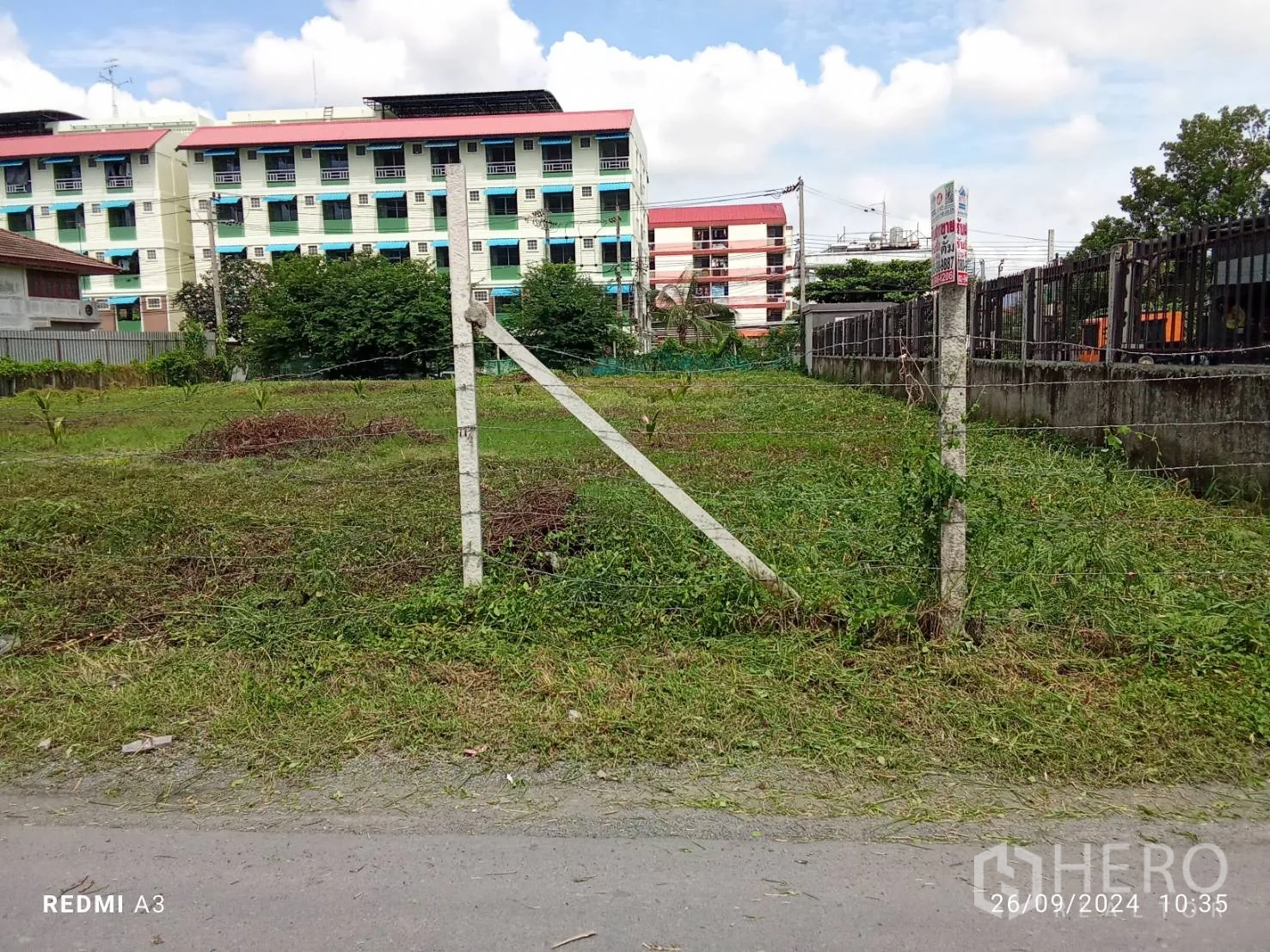 地 出租在Khan Na Yao, Bangkok - 入口立柱与铁丝门通向空地，背景可见公寓建筑。