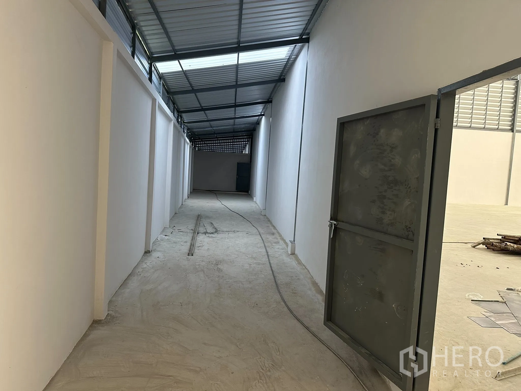 Factory for rent in Nong Khaem, Bangkok - Covered side corridor with metal roofing, white walls and a secure steel door beside the warehouse.