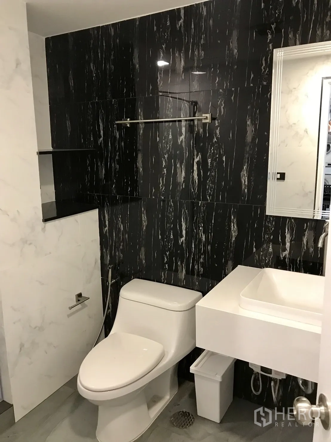 Condominium for rent or sale in Khlong Toei, Bangkok - Second bathroom featuring black accent wall, white toilet and wall-hung vanity with mirror.
