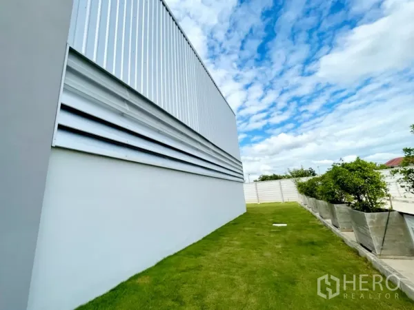 Warehouse for sale in Lam Luk Ka, Pathum Thani - Close view of warehouse exterior louver panels above a tidy grass strip and planters.