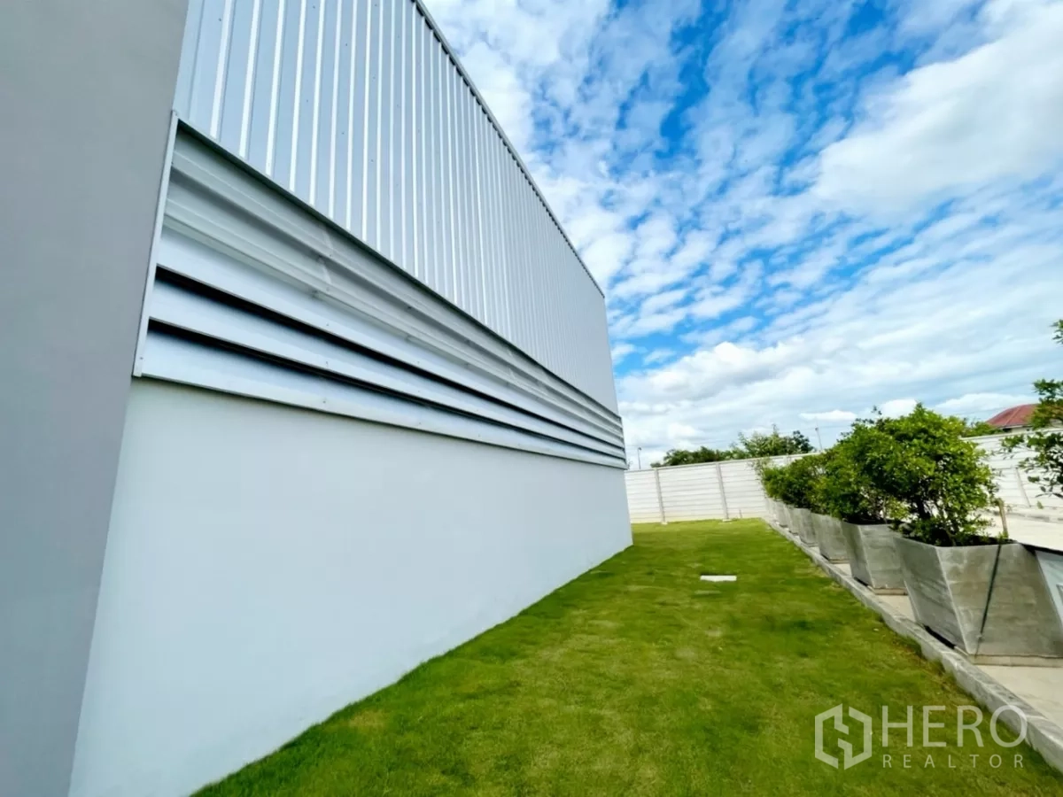 Warehouse for sale in Lam Luk Ka, Pathum Thani - Close view of warehouse exterior louver panels above a tidy grass strip and planters.