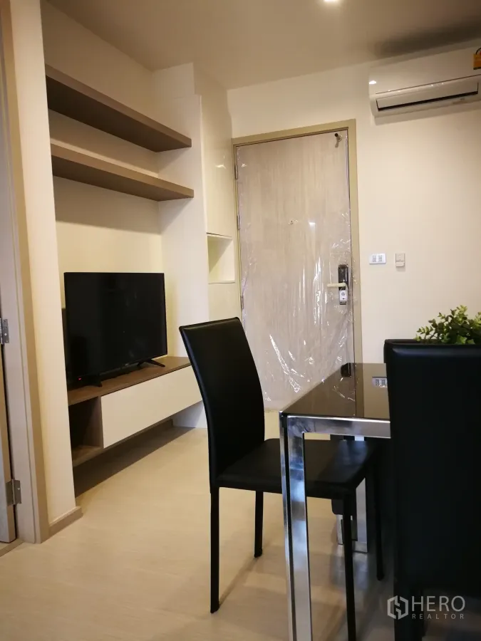 Condominium for rent in Khlong Toei, Bangkok - Compact living and dining area with wall-mounted shelves, TV console, and air conditioner.