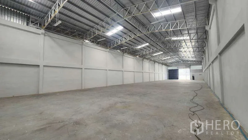 Warehouse for rent in Sam Phran, Nakhon Pathom - Long, deep warehouse aisle with steel trusses, roof skylights, and clean concrete floor leading to the entrance.