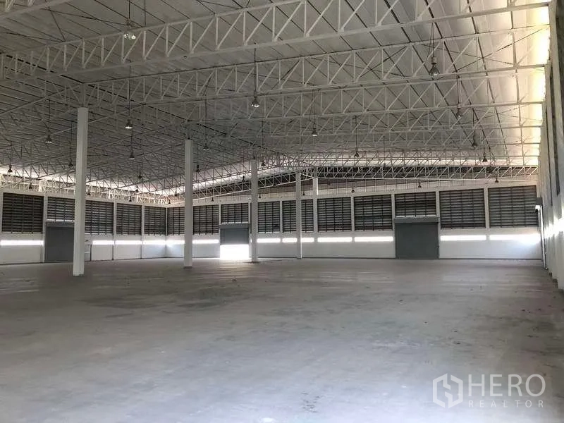 Factory for rent or sale in Phra Nakhon Si Ayutthaya - Large clear-span factory floor with hanging lights and several loading doors.