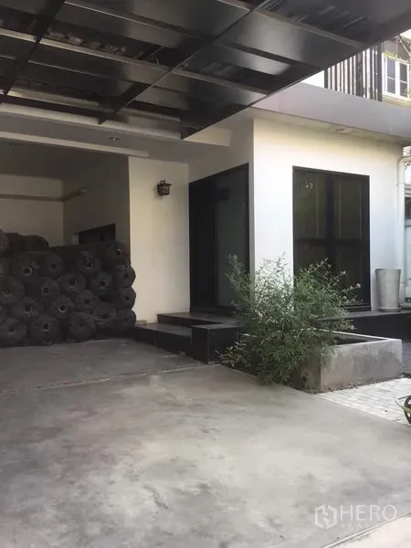 Home Office for rent in Suan Luang, Bangkok - Covered carport and main entrance with concrete driveway and small plants.