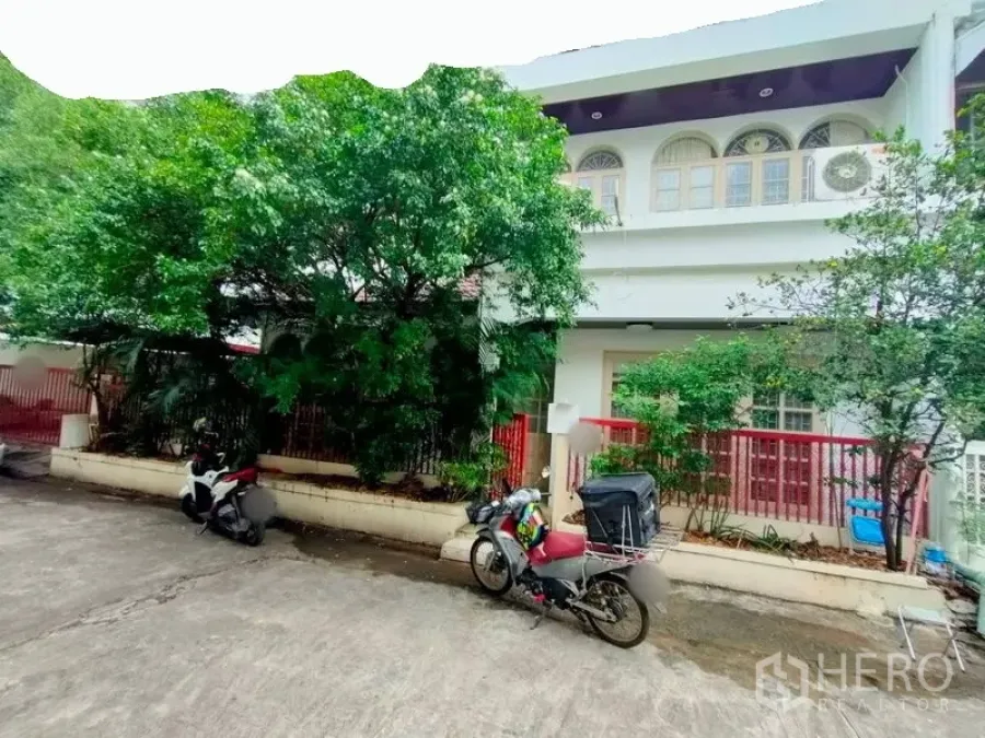 Townhouse for rent in Khlong Toei, Bangkok - Two-storey townhouse exterior with arched upper windows, red fence and mature trees on a quiet lane.