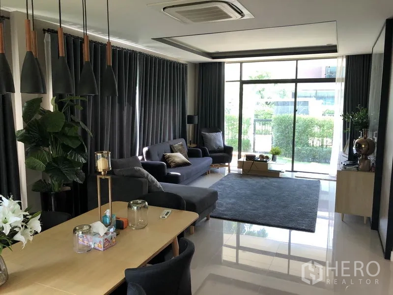 Detached House for rent in Bang Kapi, Bangkok - Living room with floor-to-ceiling glass doors, dark drapes, sofas and a large area rug.