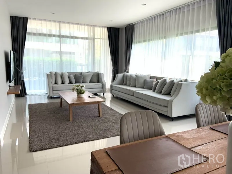 Detached House for rent or sale in Bang Kapi, Bangkok - Bright living room with two grey sofas, floor-to-ceiling windows and a dining area.