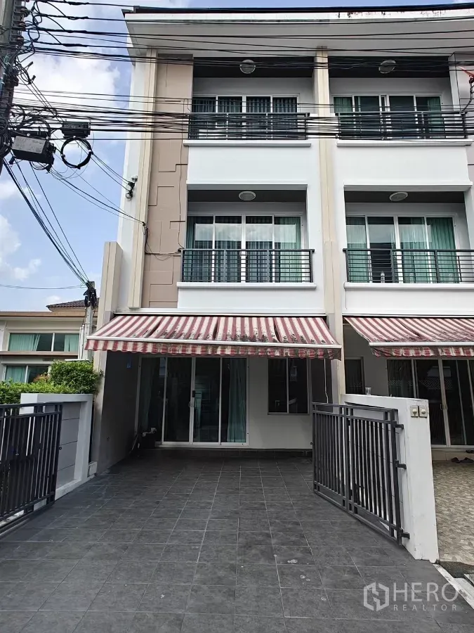 Townhouse for rent or sale in Lat Phrao, Bangkok - Three-storey modern townhouse exterior with gated driveway and striped awning in Lat Phrao.