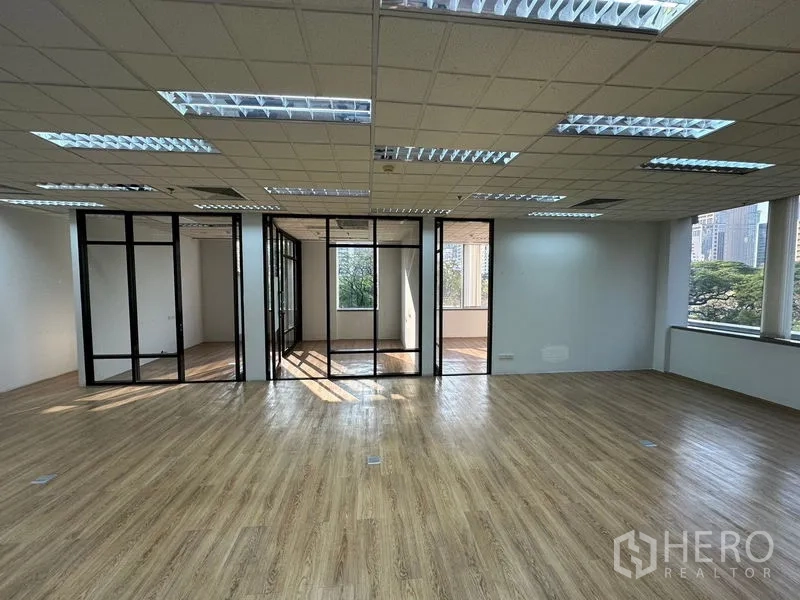 Office Space for rent - Open-plan Bangkok office with wood floors, grid ceiling lights, and glass-partitioned meeting rooms facing greenery.