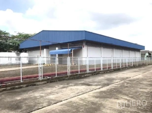 Factory for rent in Bang Bua Thong, Nonthaburi - Standalone warehouse with blue metal roof and perimeter fence.