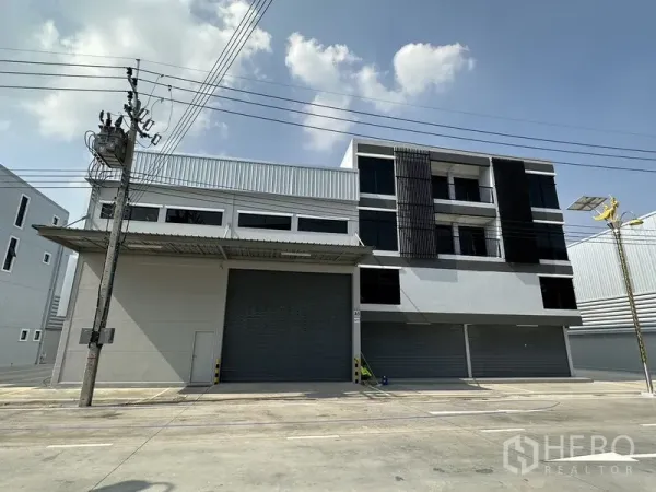 Warehouse for rent in Bang Phli, Samut Prakan - Street view of warehouse facade featuring a covered loading bay and a large grey shutter door.
