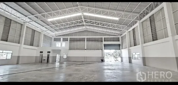 Factory for rent in Mueang Samut Prakan, Samut Prakan - Spacious factory hall with high steel truss roof, skylights, and a large roller shutter entrance.