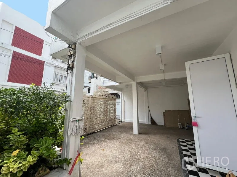 Home Office for rent in Watthana, Bangkok - Covered carport with white columns beside greenery and a decorative lattice gate.