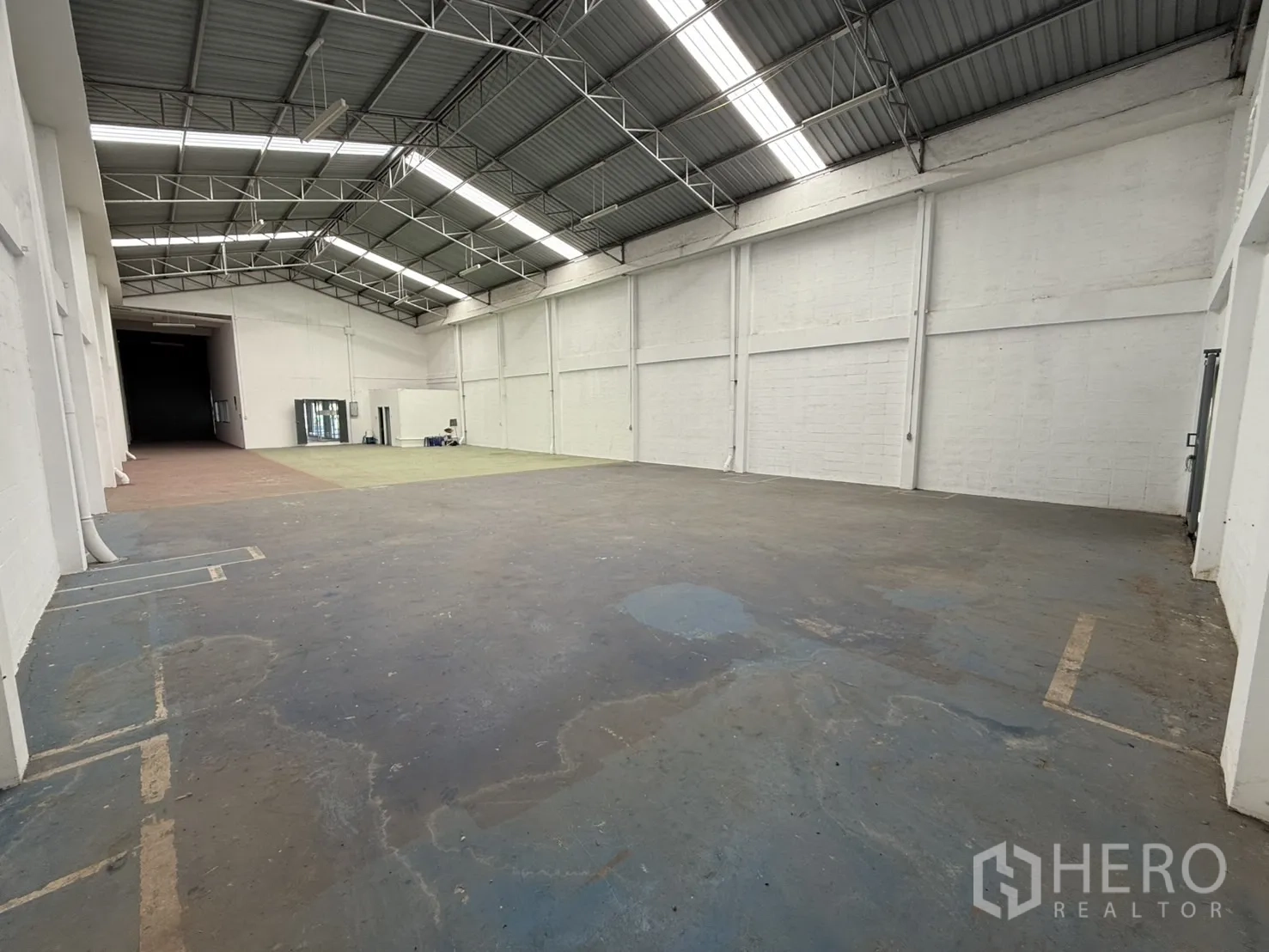Warehouse for rent in Bang Phli, Samut Prakan - Spacious open-plan warehouse interior with a high steel-truss roof, skylight panels, white walls and durable concrete floor.