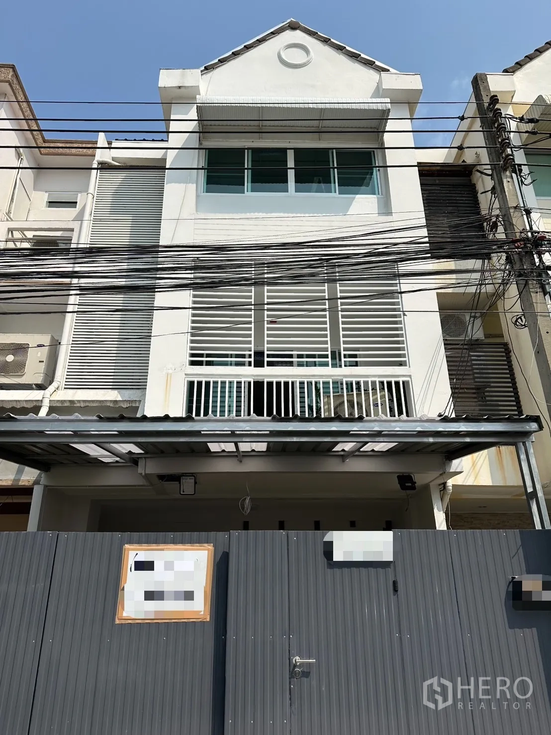 Townhouse for rent in Watthana, Bangkok - Three-storey white townhouse facade with gated entry and balcony screens.