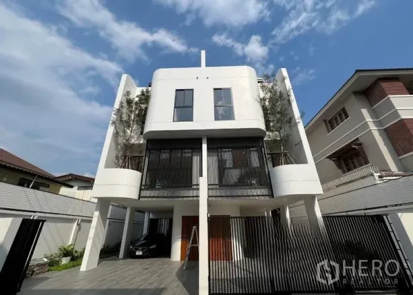 Home Office for sale in Phra Khanong, Bangkok - Modern three‑storey home office with gated driveway and covered parking under cantilevered upper floors.