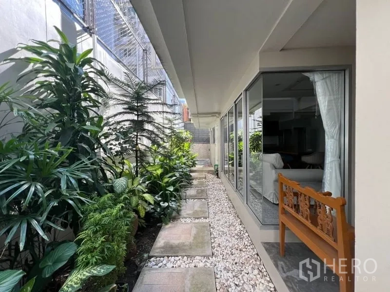 联排别墅 出租在Khlong Toei, Bangkok - 房屋侧面花园步道，热带绿植与落地玻璃墙相伴。