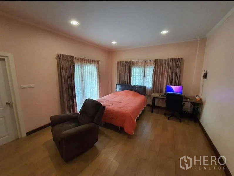 Detached House for sale in Sai Mai, Bangkok - Ground-floor bedroom with pink walls, corner windows, desk and reclining chair.